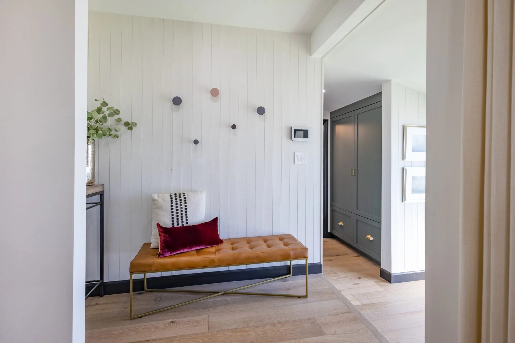 Minimalist entryway with a tufted bench, accent pillows, and light wood flooring