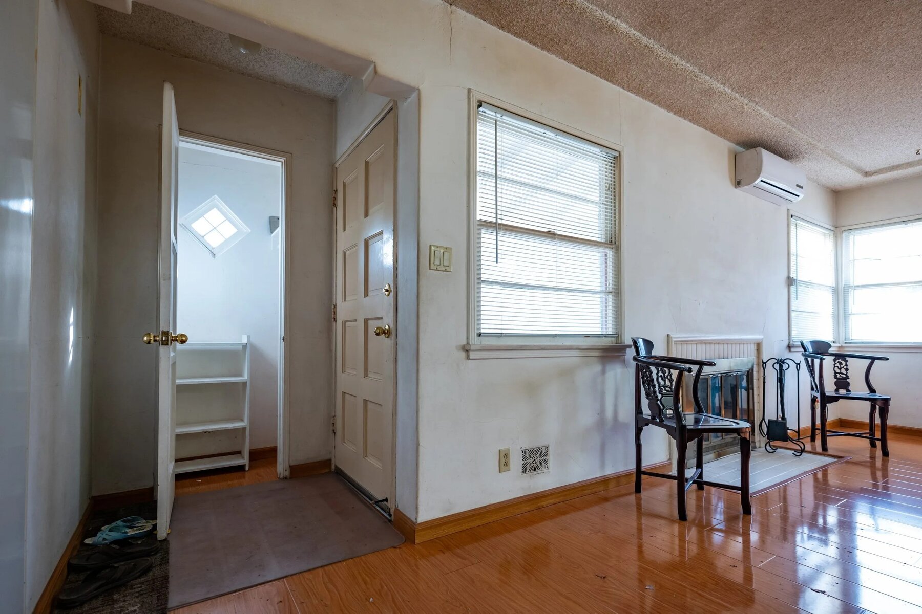Empty room with wooden floors, a door to a small closet, chairs, and windows with blinds