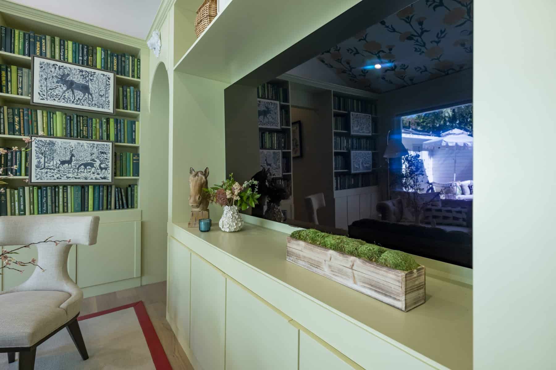 Home library with green built-in bookshelves decorative artwork and a large reflective mirror