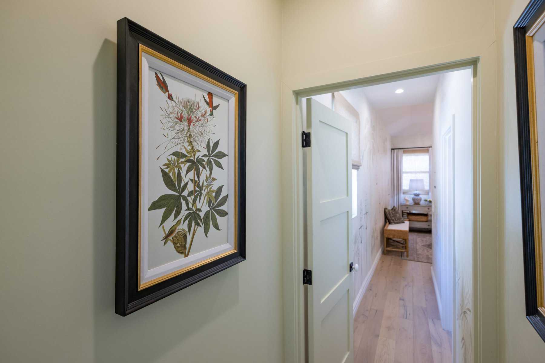 Hallway with botanical artwork on the wall, leading to a cozy room with natural light and a wooden bench