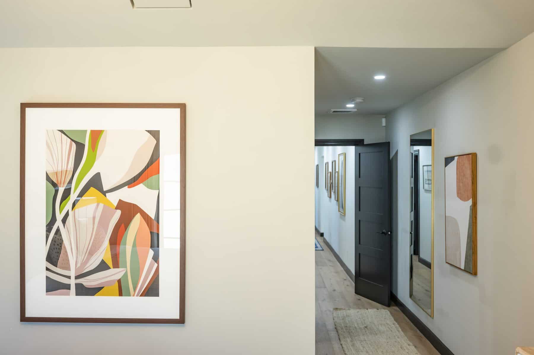 Hallway with abstract artwork, a large mirror, and a black door leading to another room