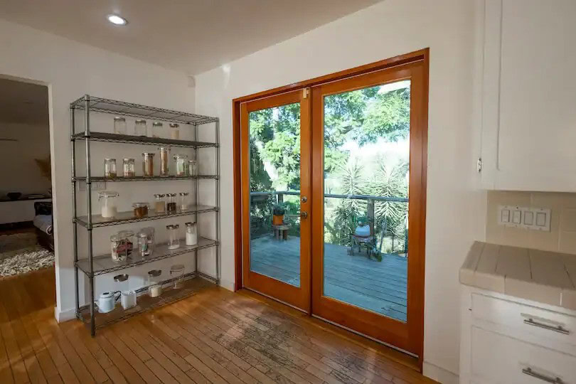 Kitchen with a metal shelving unit filled with jars and double doors leading to a deck