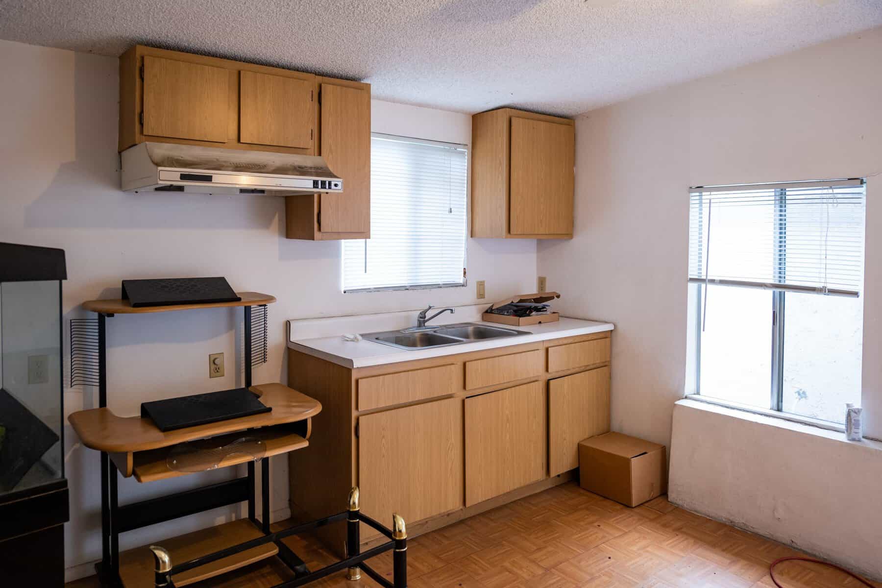 Small outdated kitchen with wooden cabinets, a double sink, and minimal furnishings