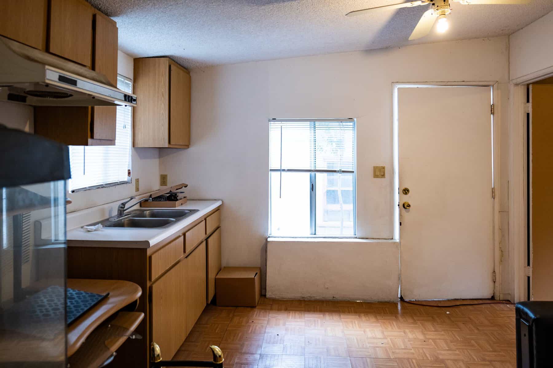 Basic kitchen with wood cabinets, a double sink, and minimal furnishings in a small, dimly lit space