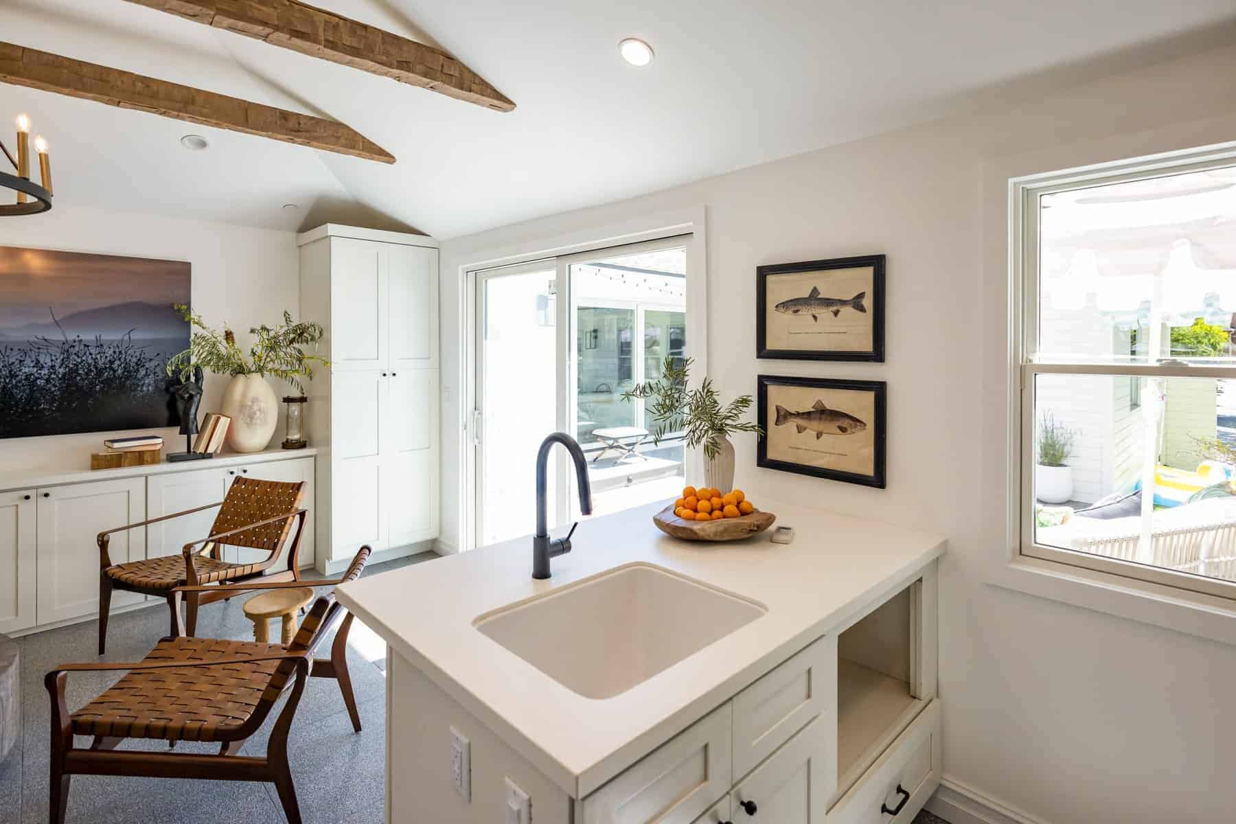 Bright kitchen lounge with vaulted ceiling, wood beams, woven chairs, and white island topped with oranges