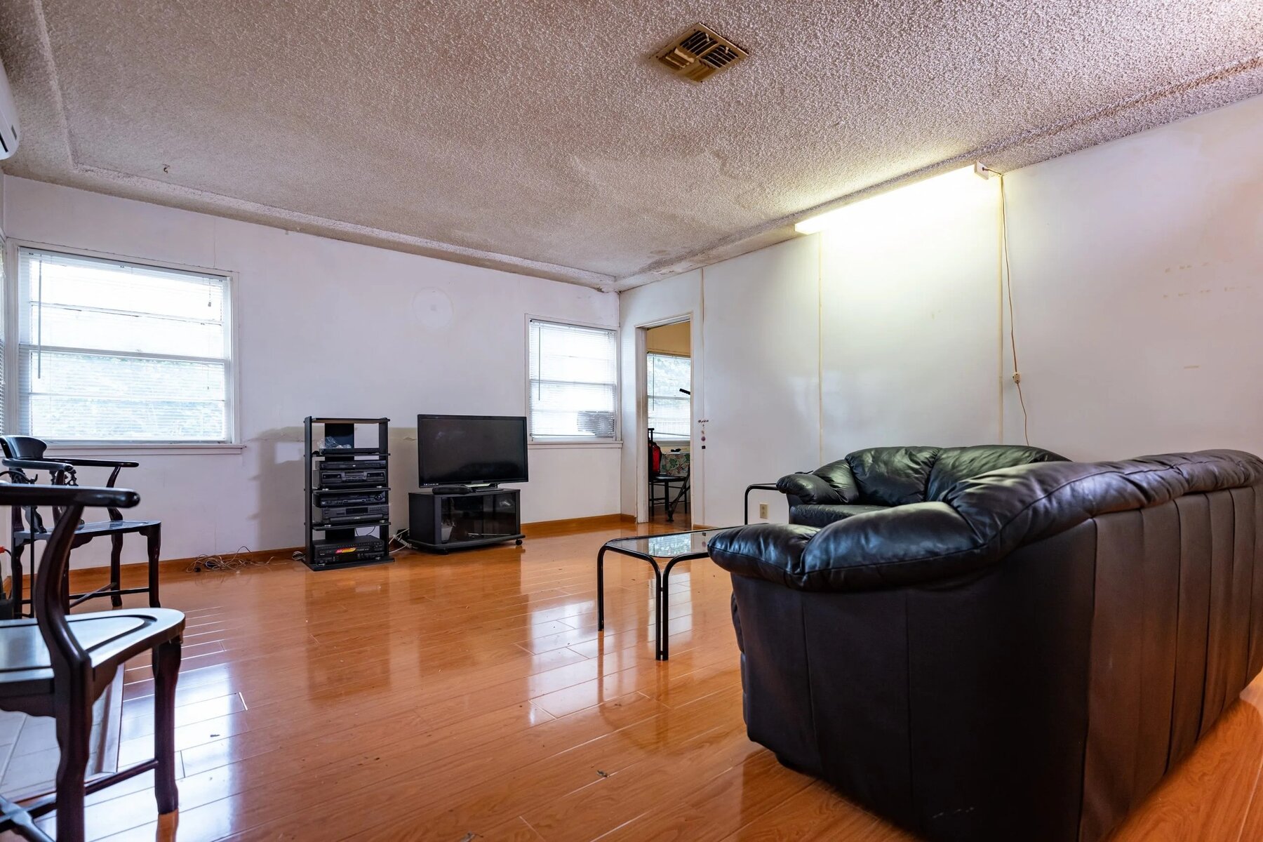 Living room with black leather sofas, a small glass coffee table, and a TV stand against plain white walls