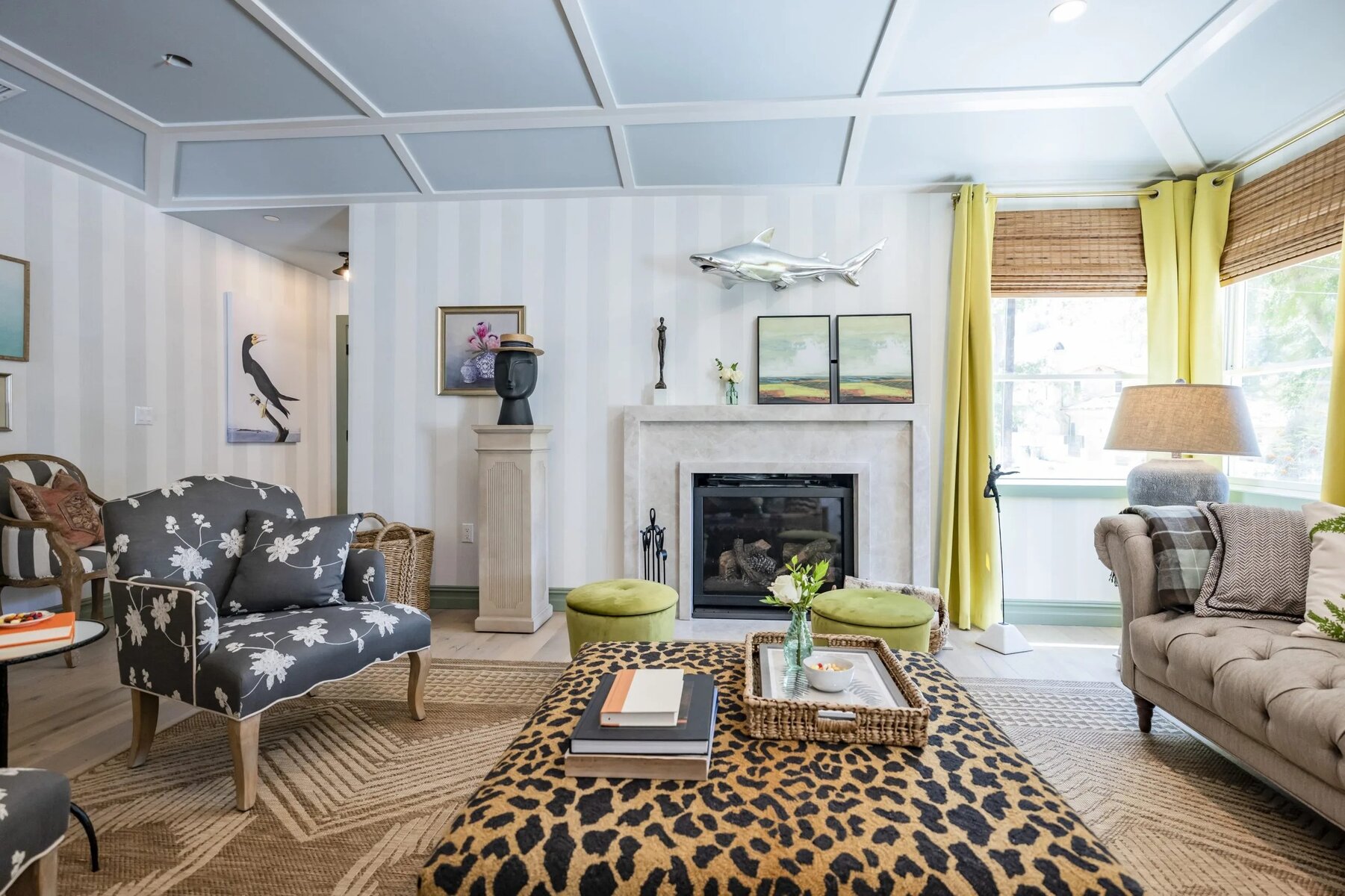 A coastal-themed living room with a light blue striped wall, a coffered ceiling, and a white marble fireplace