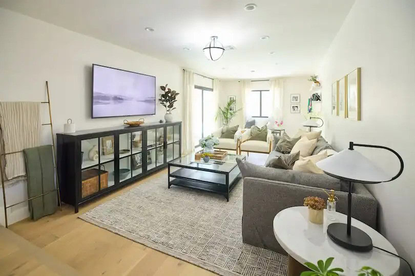 Bright living room with neutral tones, cozy seating, and a large wall-mounted TV