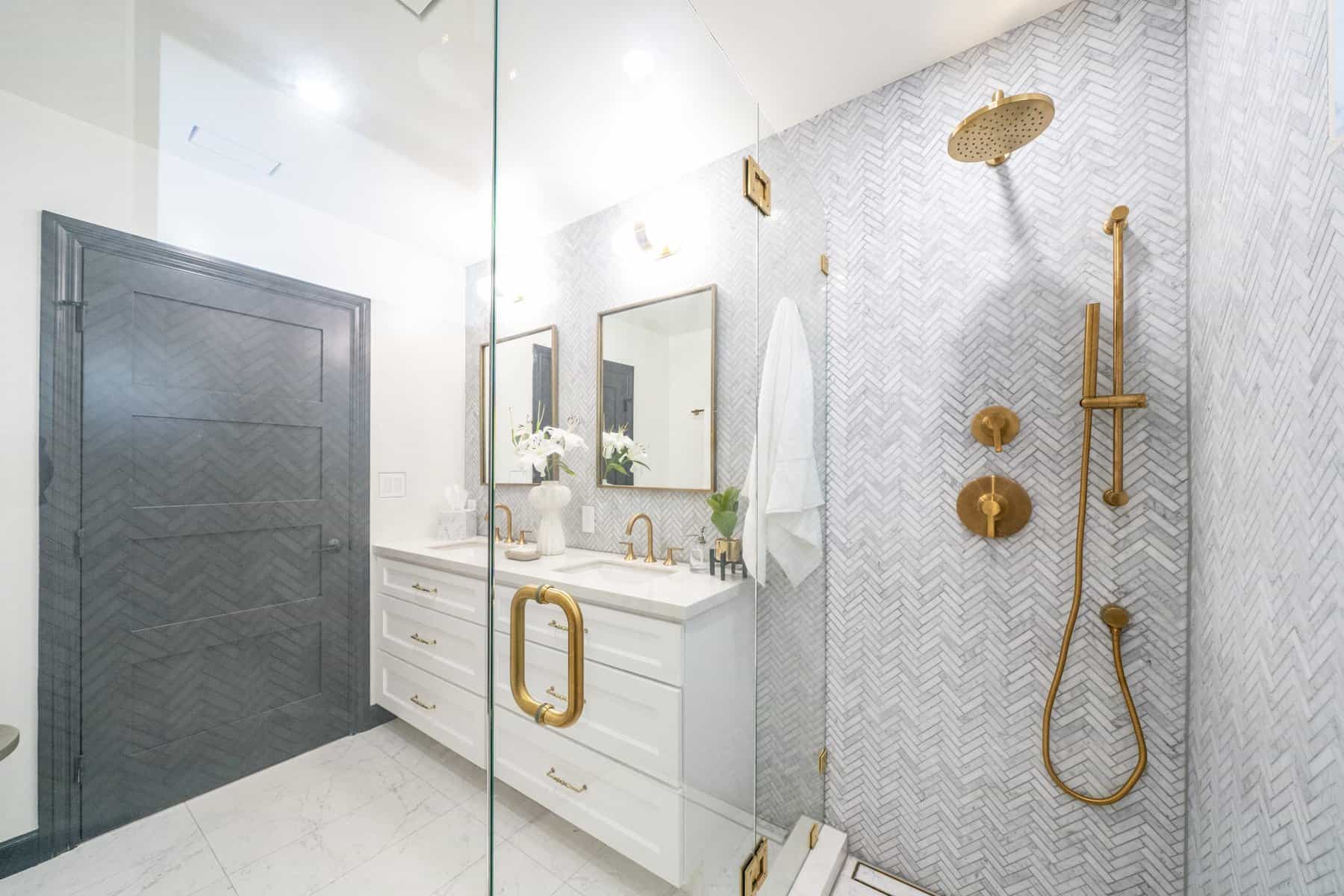 Modern bathroom with gold fixtures, double vanity, and herringbone tile shower