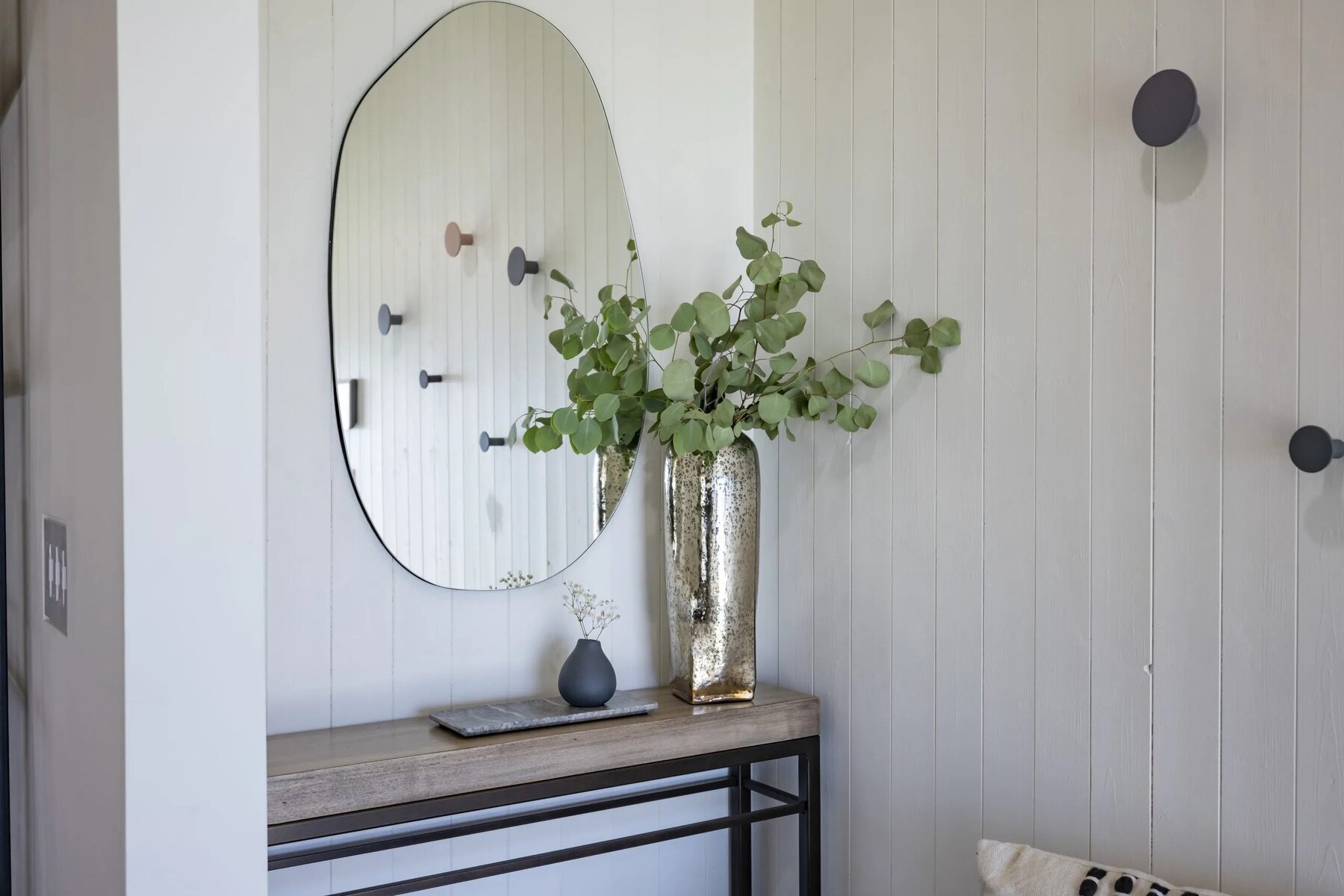 Entryway table with a decorative mirror, metallic vase with greenery, and minimal decor