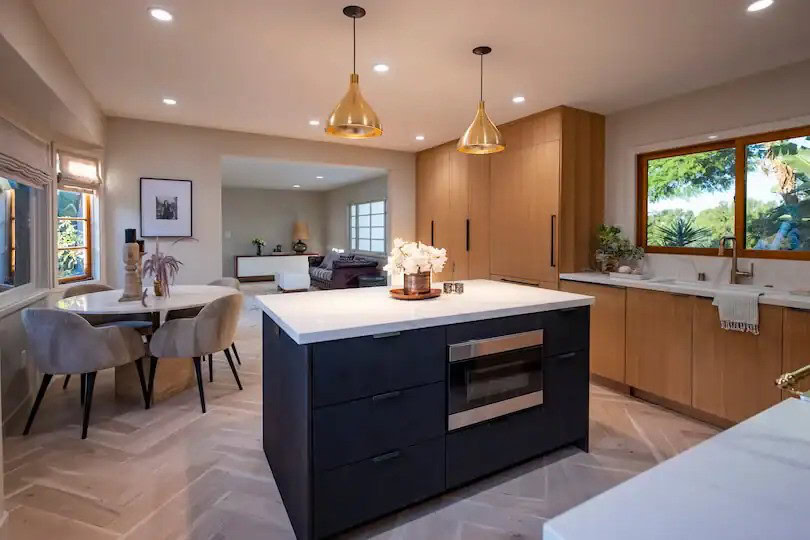 Kitchen with a black island, wood cabinets, gold pendant lights, and a dining table with beige chairs