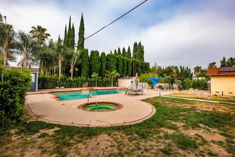 Spacious backyard with a swimming pool, hot tub, and lush greenery