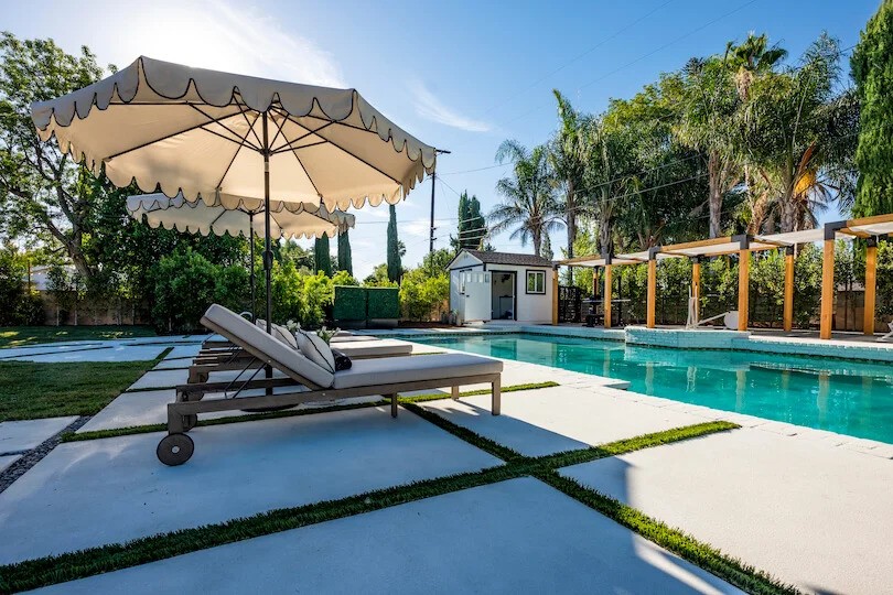 Poolside patio with lounge chairs under scalloped umbrellas, surrounded by palm trees and greenery