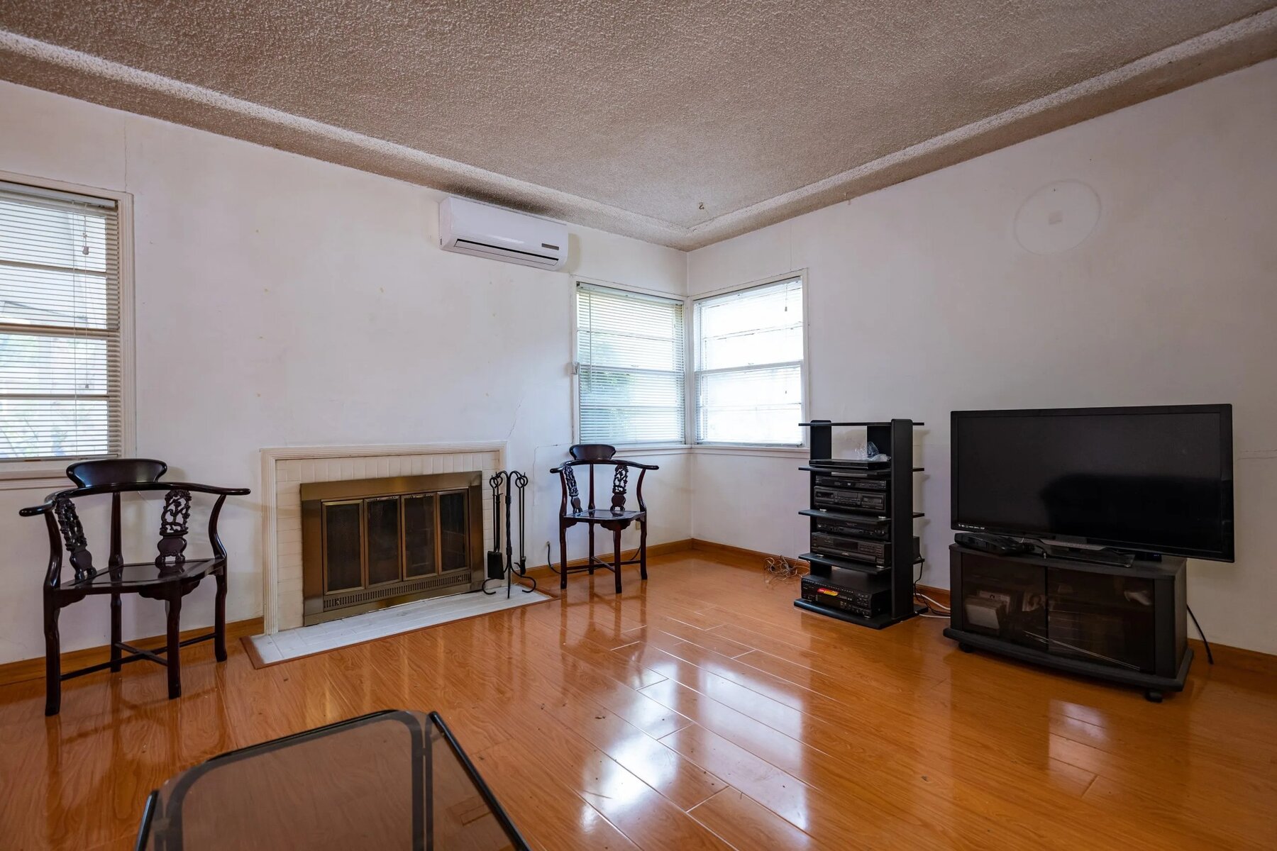 Simple living room with wood flooring, fireplace, TV, stereo system, and two wooden chairs