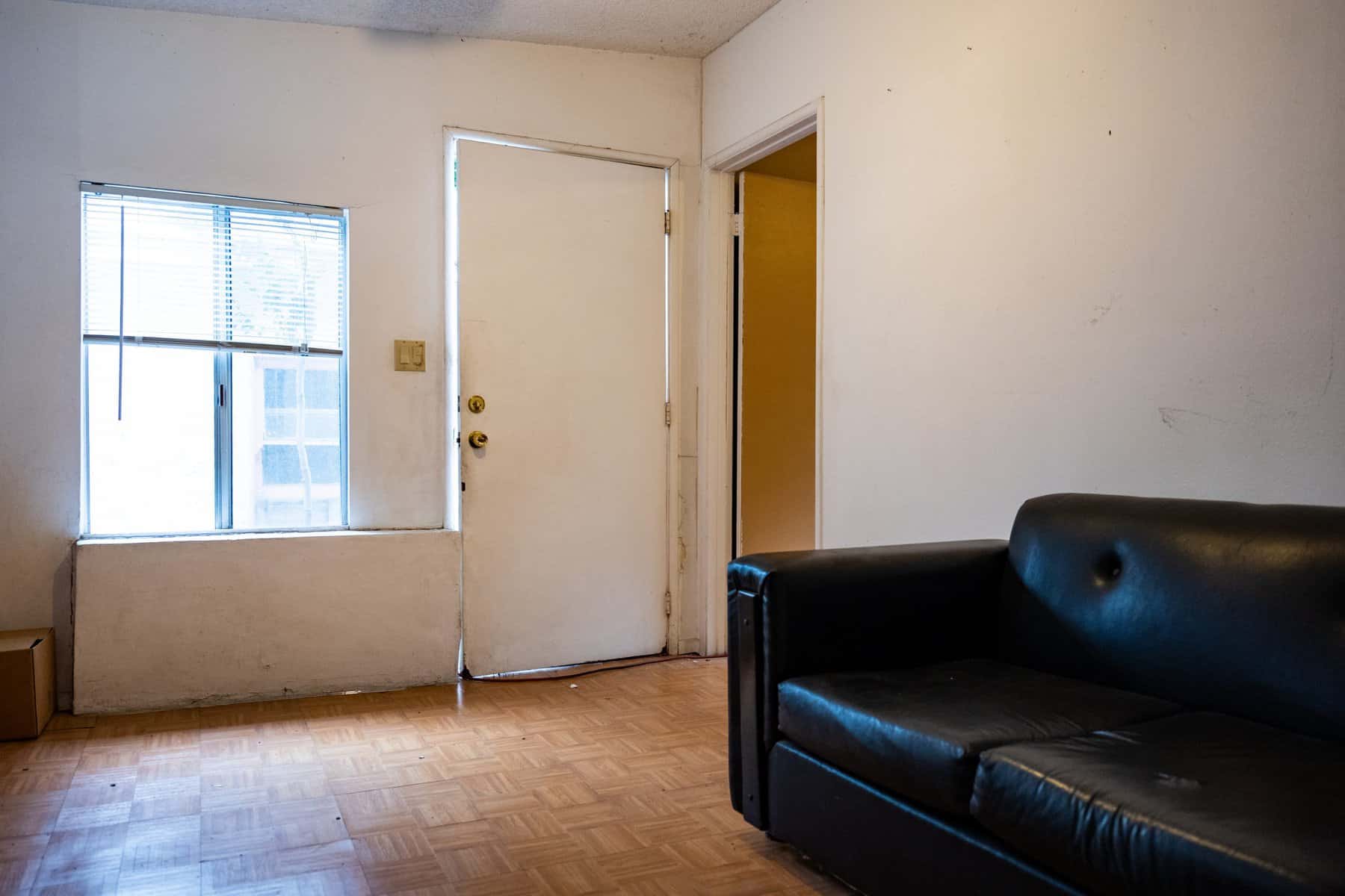 Minimalist living space with a black leather couch, a white door, and a window with blinds