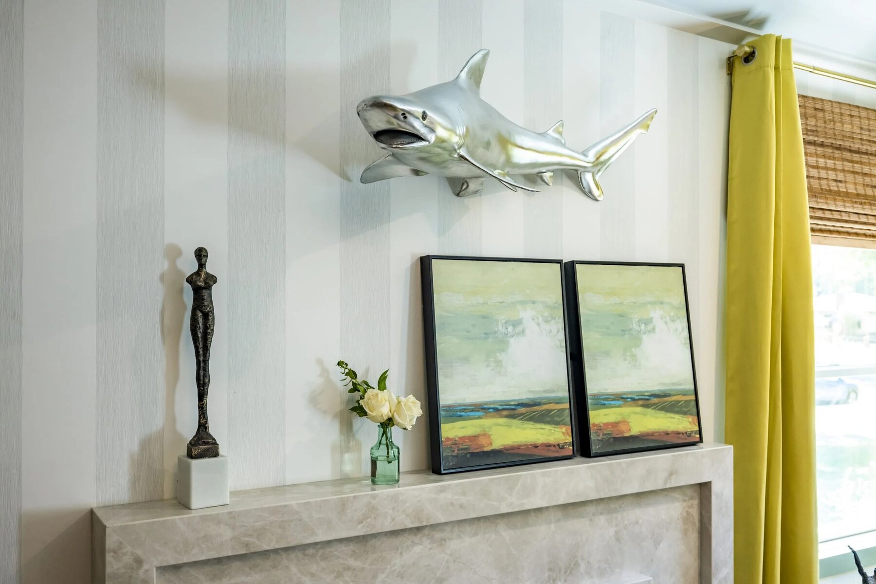 Mantel with a sculpture, framed artwork, a vase of flowers, and a mounted shark decor above