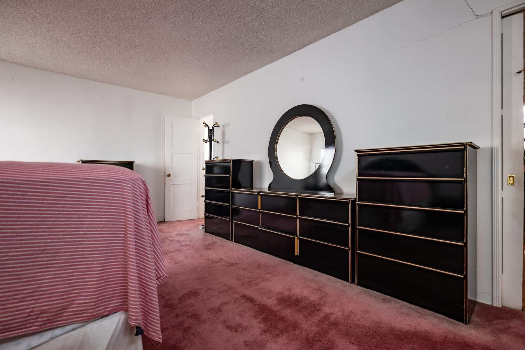 Bedroom with a bed covered in a pink and black striped blanket, a large black dresser with a mirrored top, and a carpeted floor