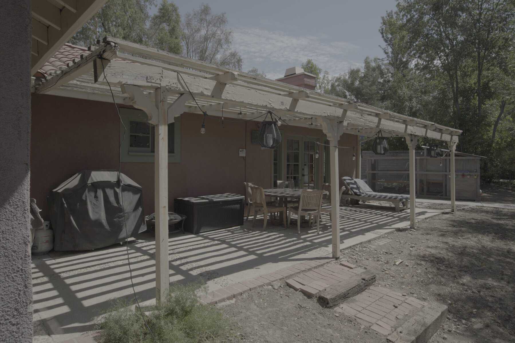 Outdoor patio with a weathered pergola, dining area, and lounge chairs