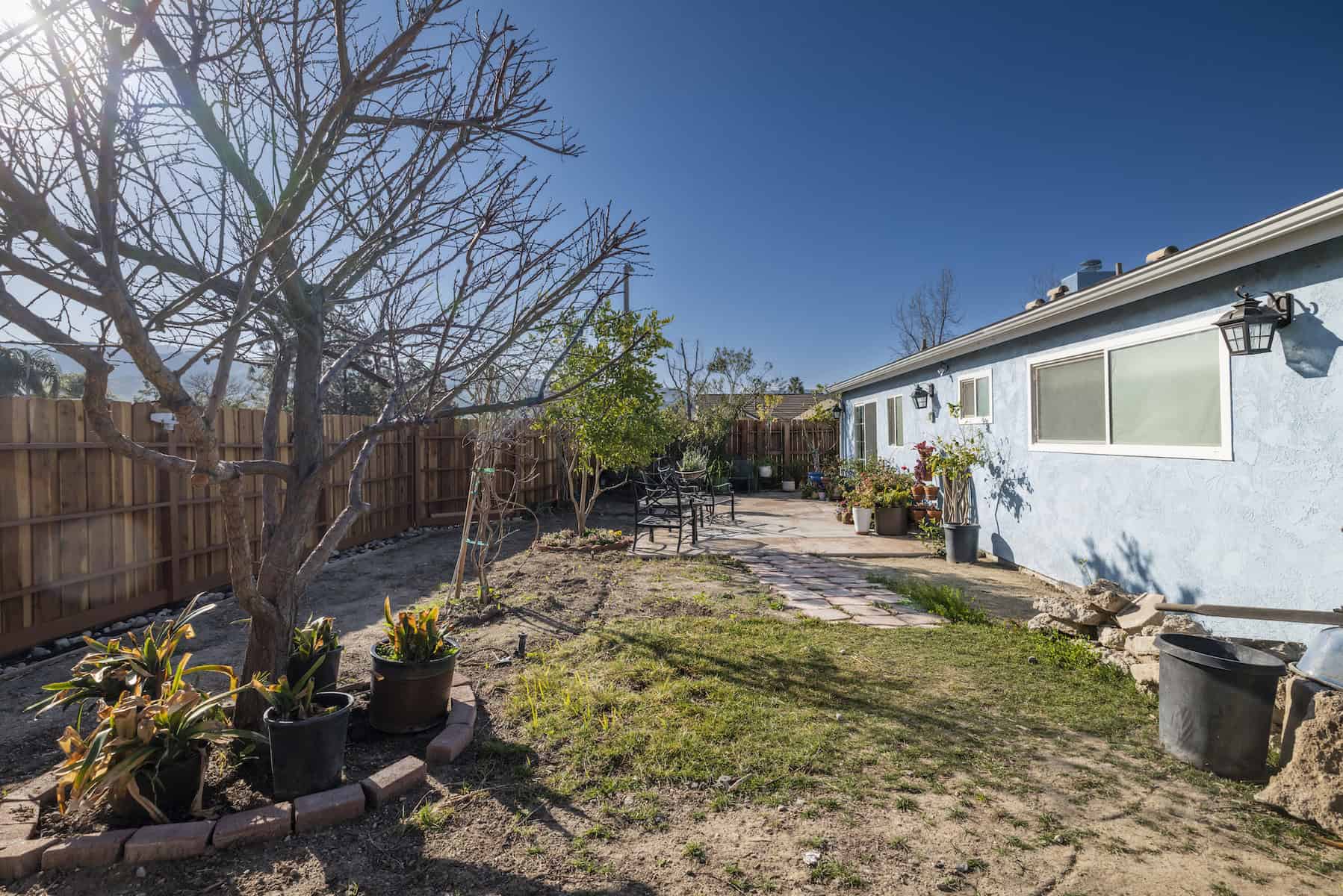Backyard with paver path, patio seating, and sparse landscaping against a blue house