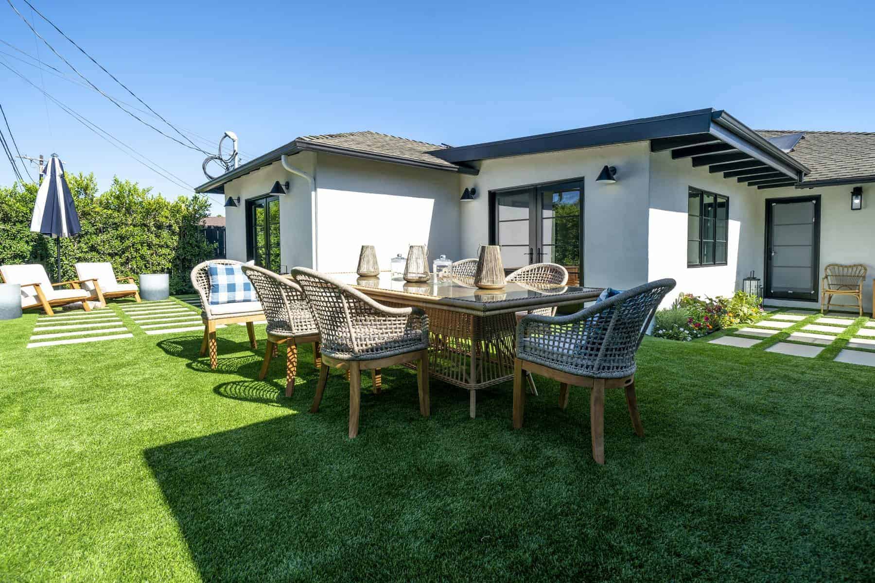 Backyard with artificial grass, wicker dining set, lounge chairs, and white modern house exterior