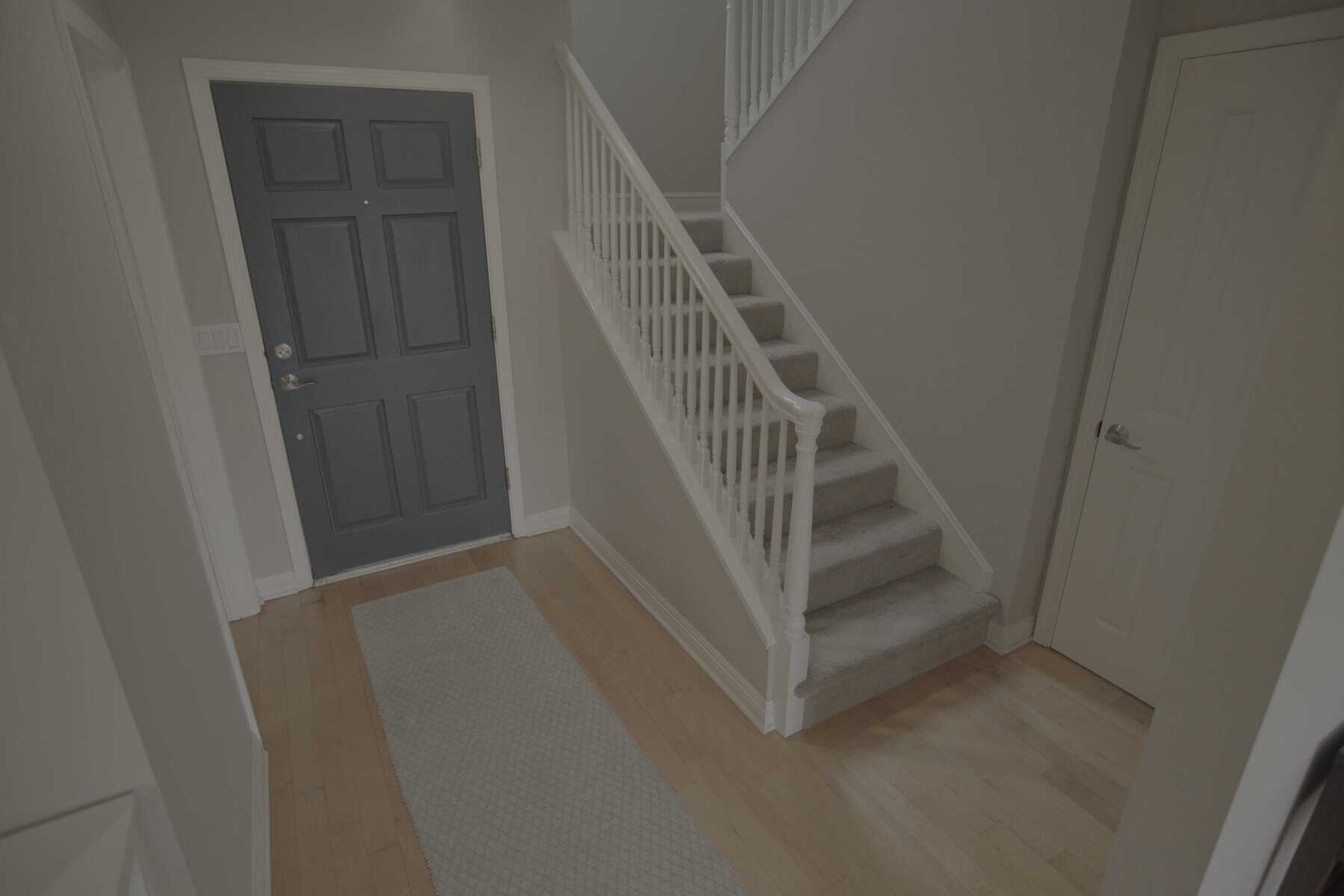 Entryway with a dark blue door, light wood floors, gray rug, and white staircase