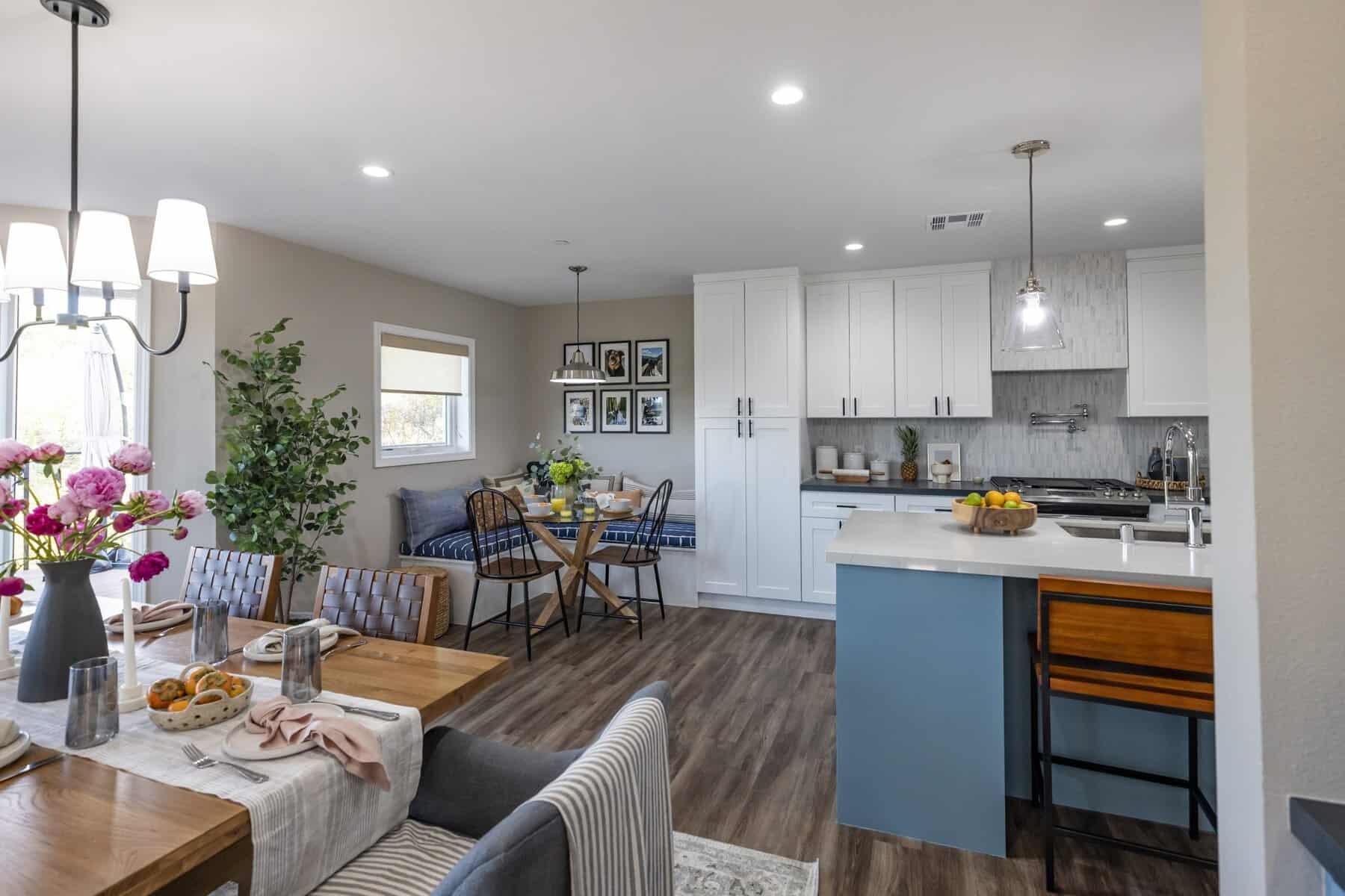 Open kitchen and dining area with white cabinets, a blue island, wood flooring, and a cozy breakfast nook