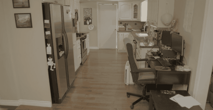 Cluttered kitchen area with a desk and office chair in the foreground