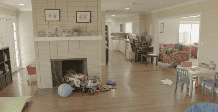 Living room with a fireplace, kids' toys scattered around, and a desk area leading to a kitchen