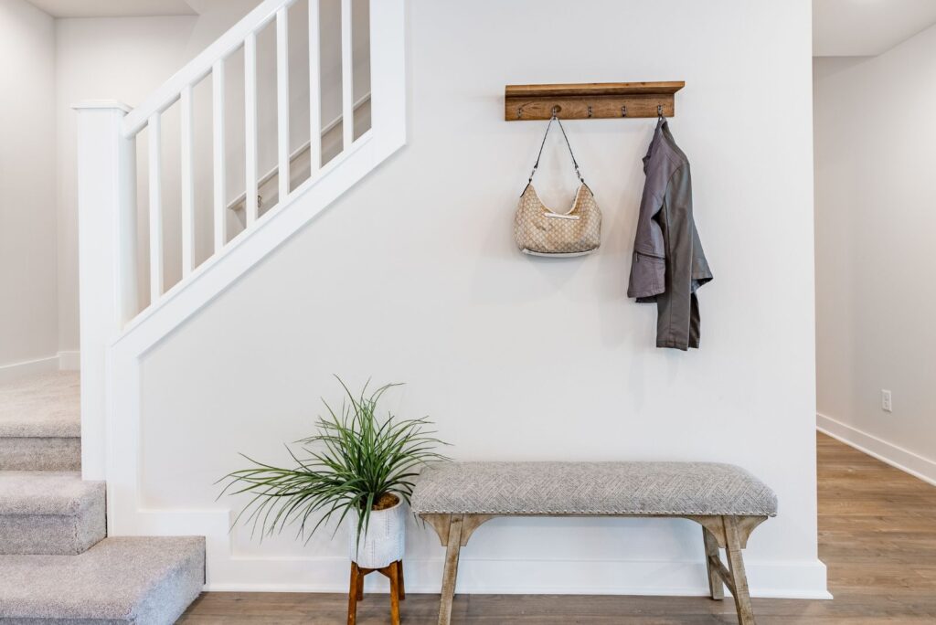 entryway along stair wall with wall shelf, coat hooks, and shoe bench