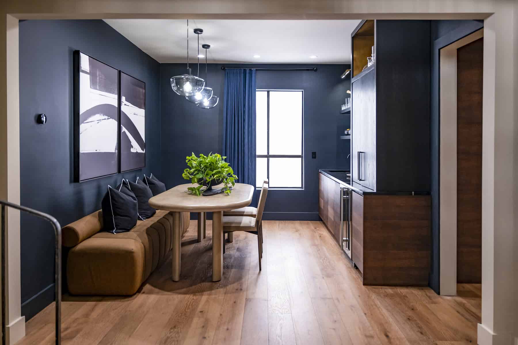 Modern dining area with dark walls, wooden table, cushioned bench, pendant lights, and a bar area