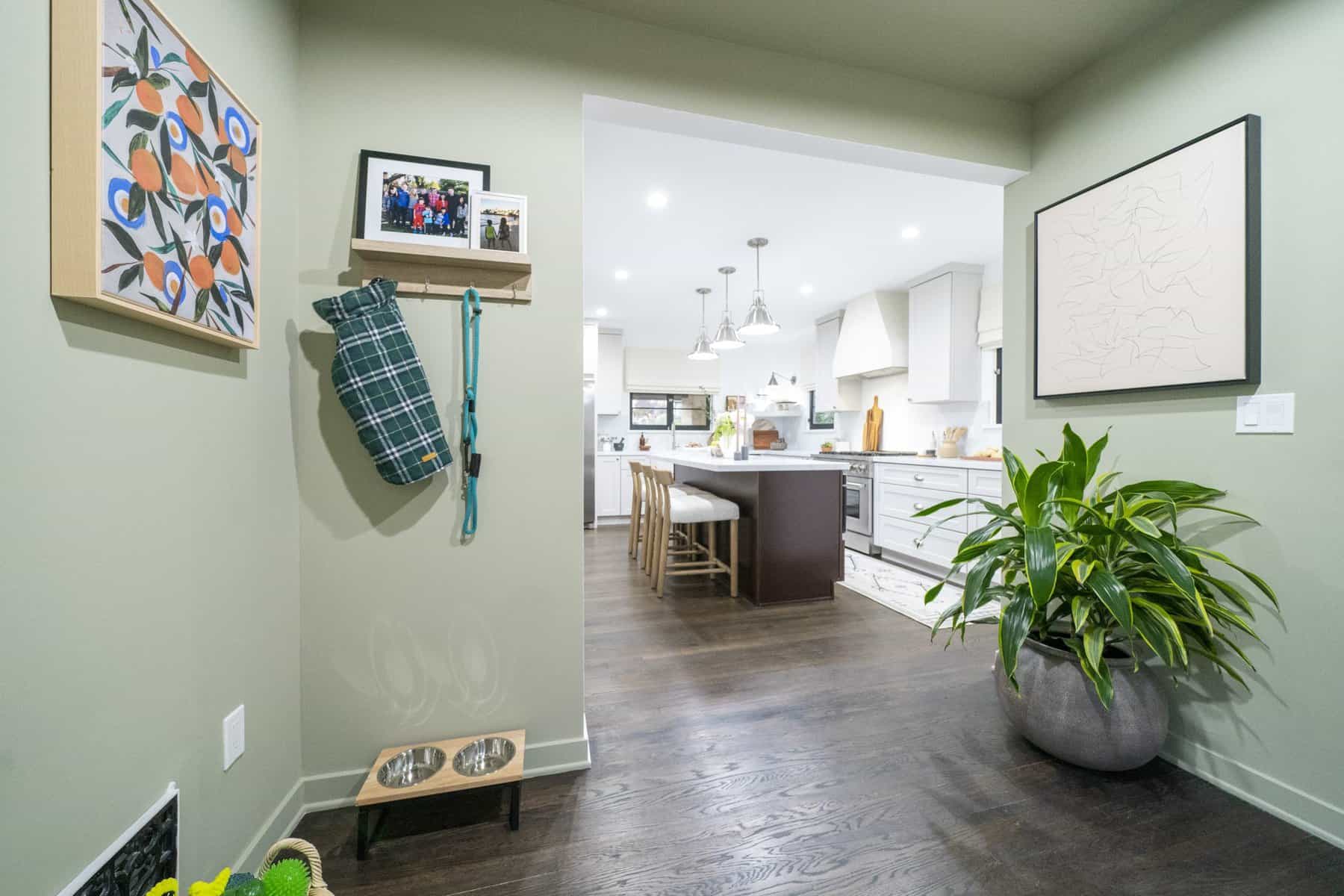 Entryway leading to a bright kitchen, with green walls, framed art, a dog leash station, and a large potted plant