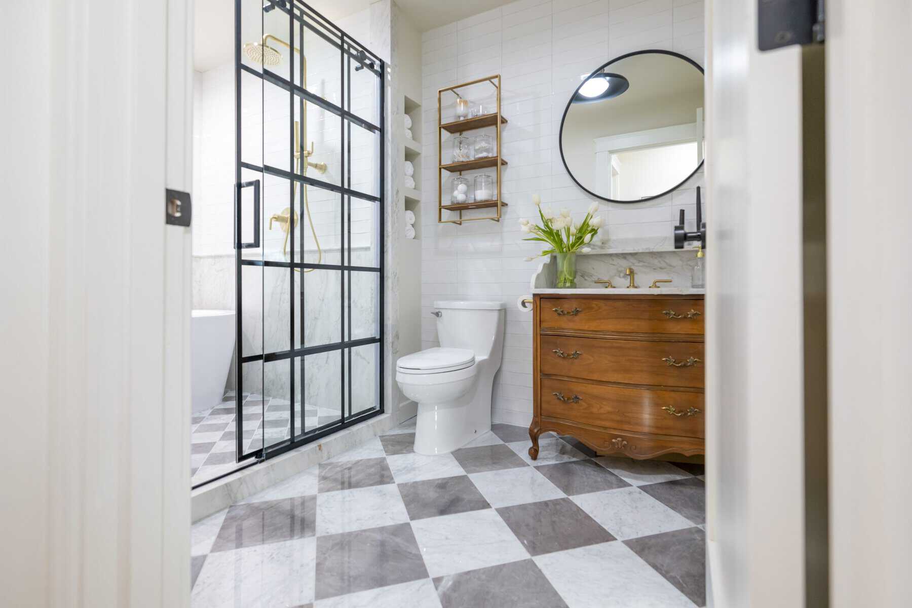 Elegant bathroom with checkered marble floor, vintage vanity, and gold-accented glass shower