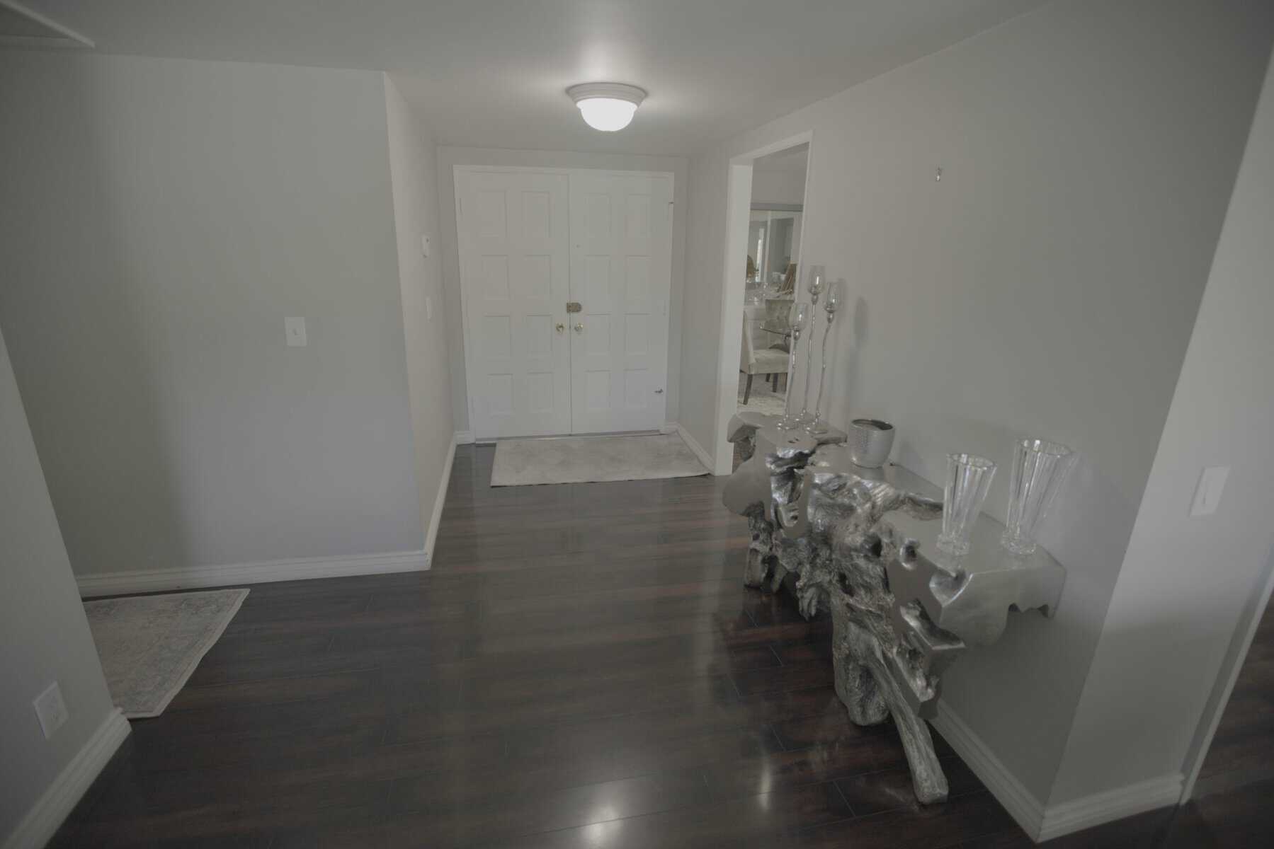 Entryway with dark wood flooring, white double doors, and a sculptural silver console table