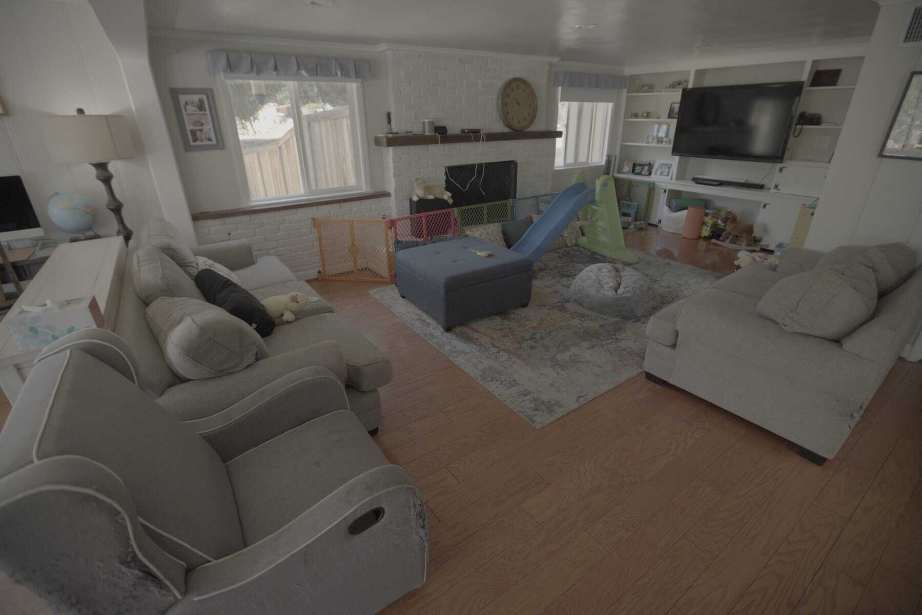 Family living room with kids’ play area, slide, light gray sofas, and a white brick fireplace