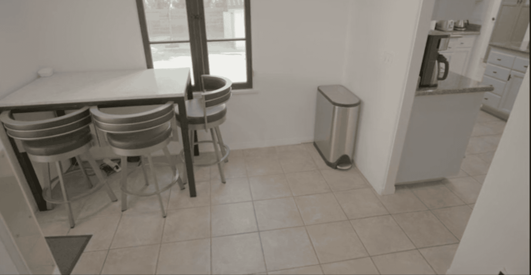 Small kitchen nook with metal barstools, marble table, and stainless steel trash bin