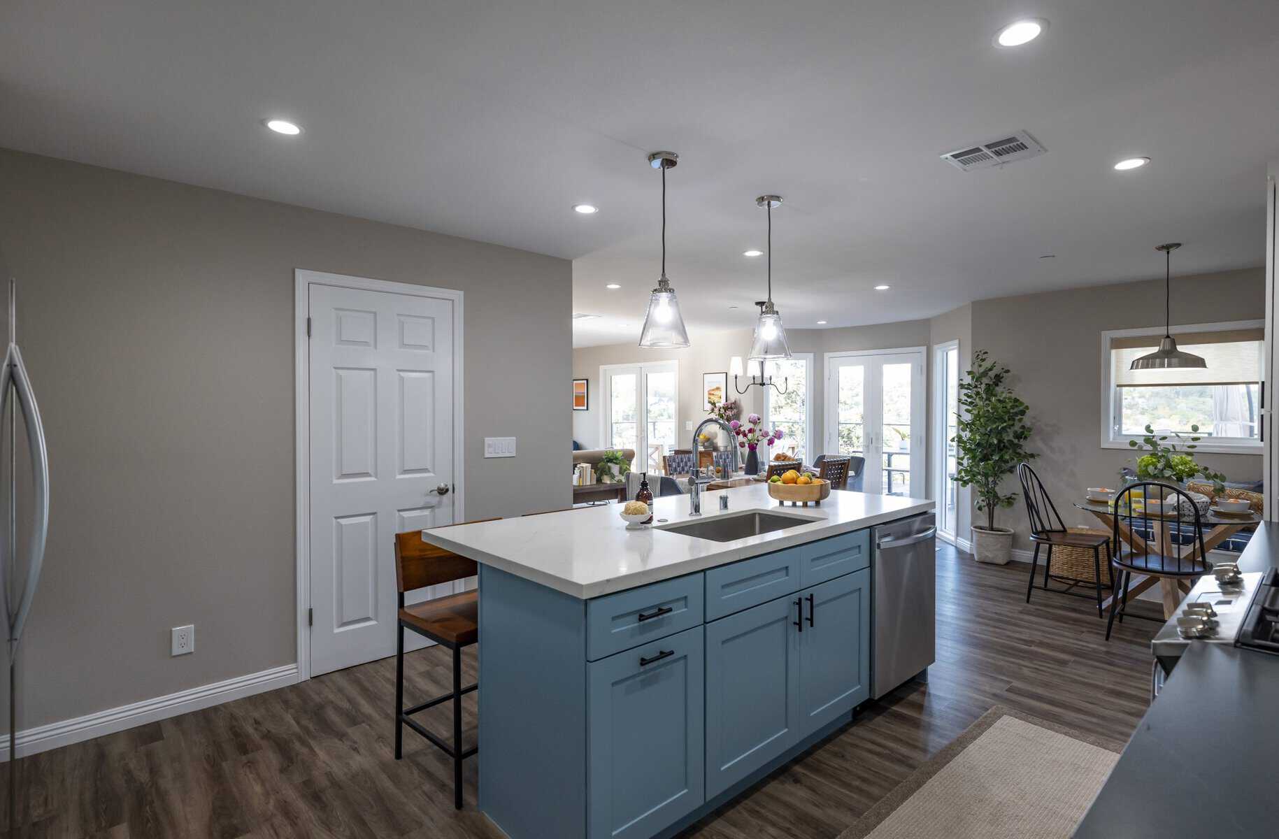 Open-concept kitchen with blue island, pendant lights, and dining area with natural light