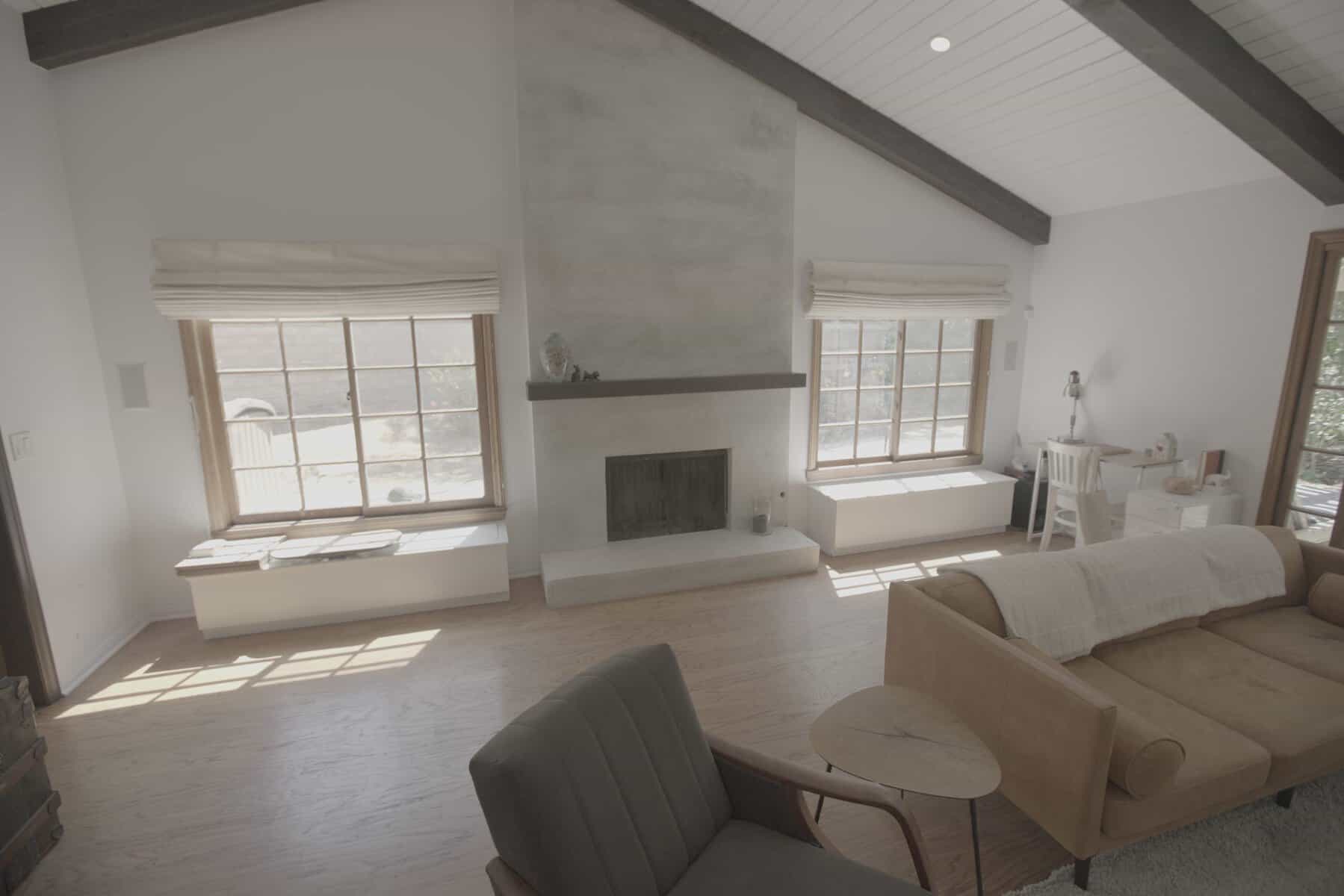 Bright living room with a fireplace, large windows, sofa, armchair, and small workspace