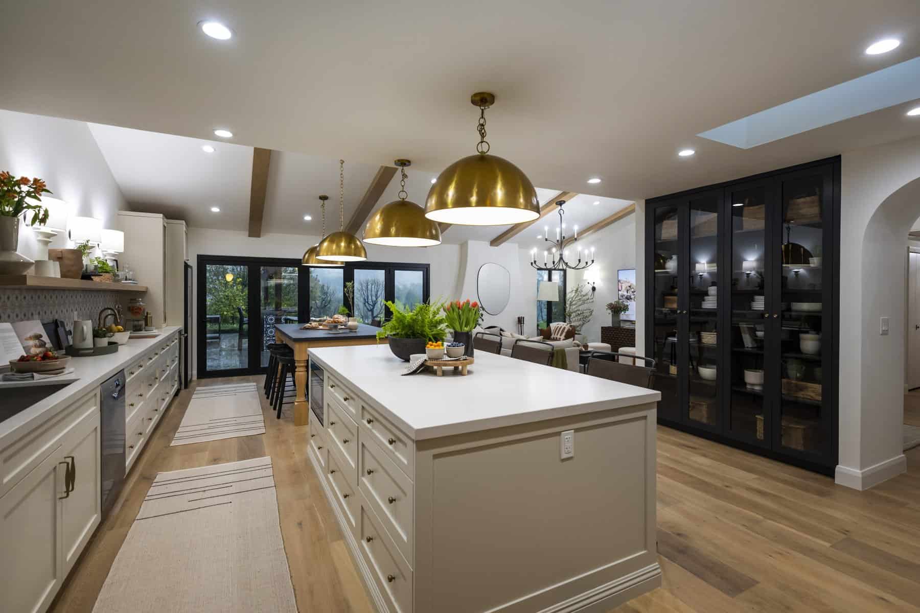 Spacious open-concept kitchen with large island, gold pendant lights, black glass cabinets, and cozy dining area