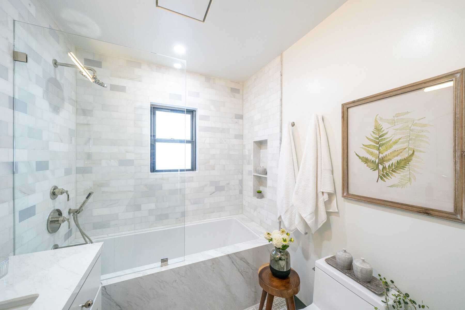 Bright bathroom with marble tile, glass shower, and botanical artwork