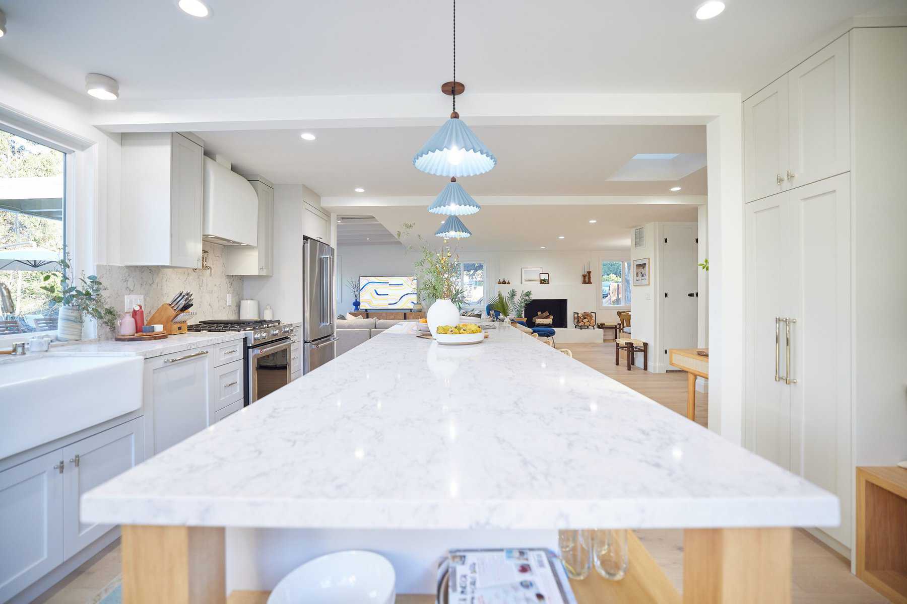 Bright open-concept kitchen with a long marble island, white cabinets, and blue pendant lights