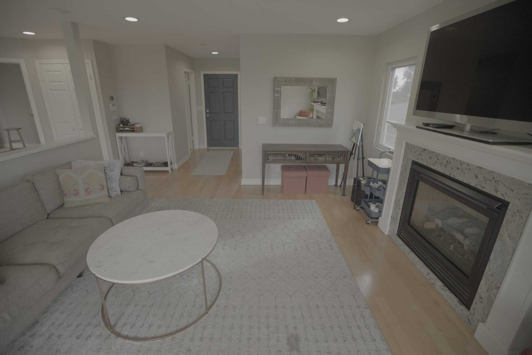 Living room with a gray sofa, marble coffee table, fireplace, and entryway featuring a console table and a blue door