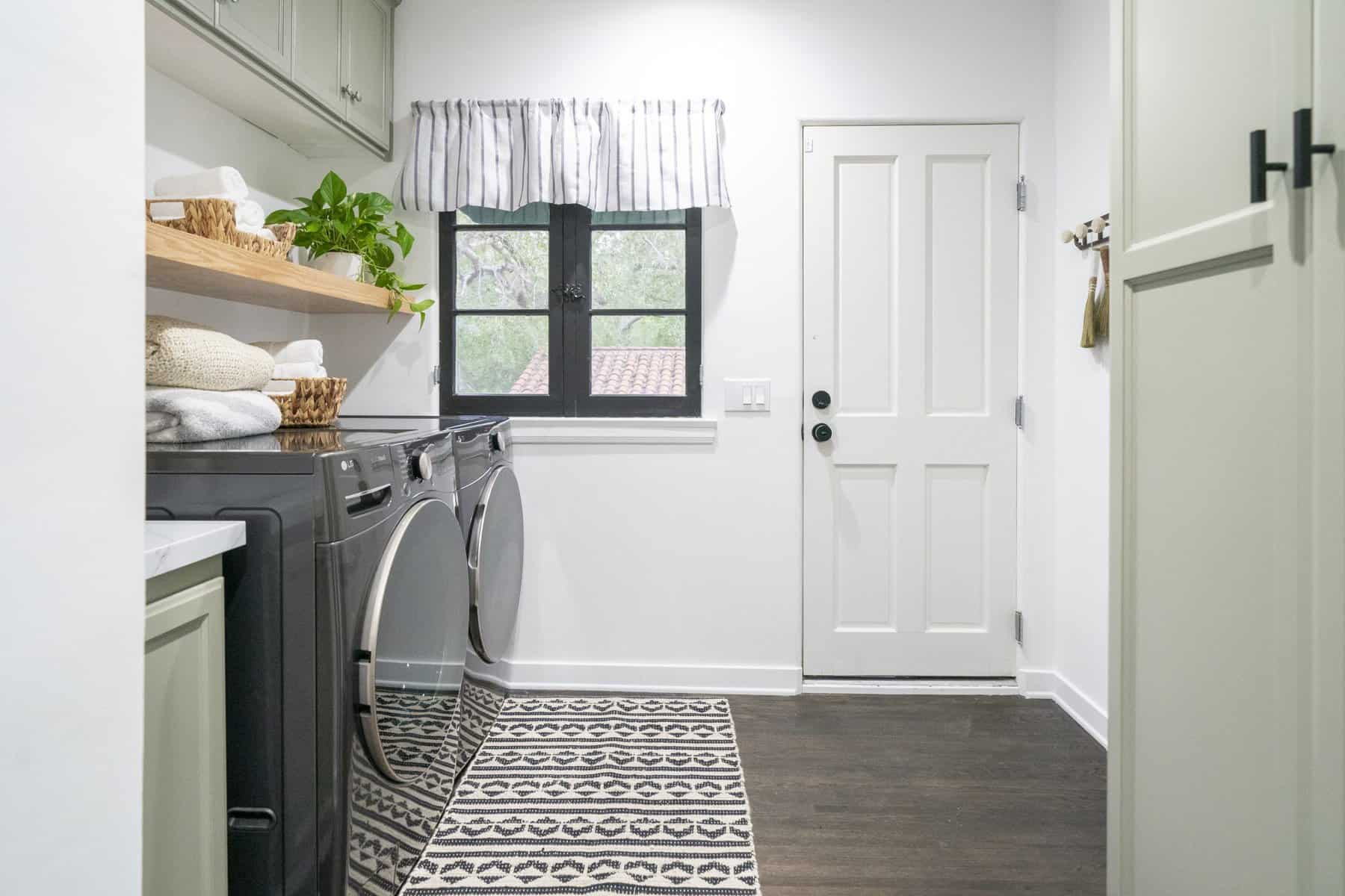 Laundry room with black machines, open shelf, and striped curtains