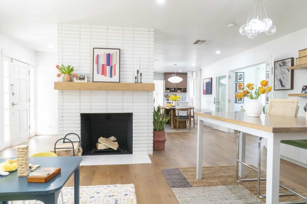 Bright open living space with a white brick fireplace, wood mantle, and modern decor accents