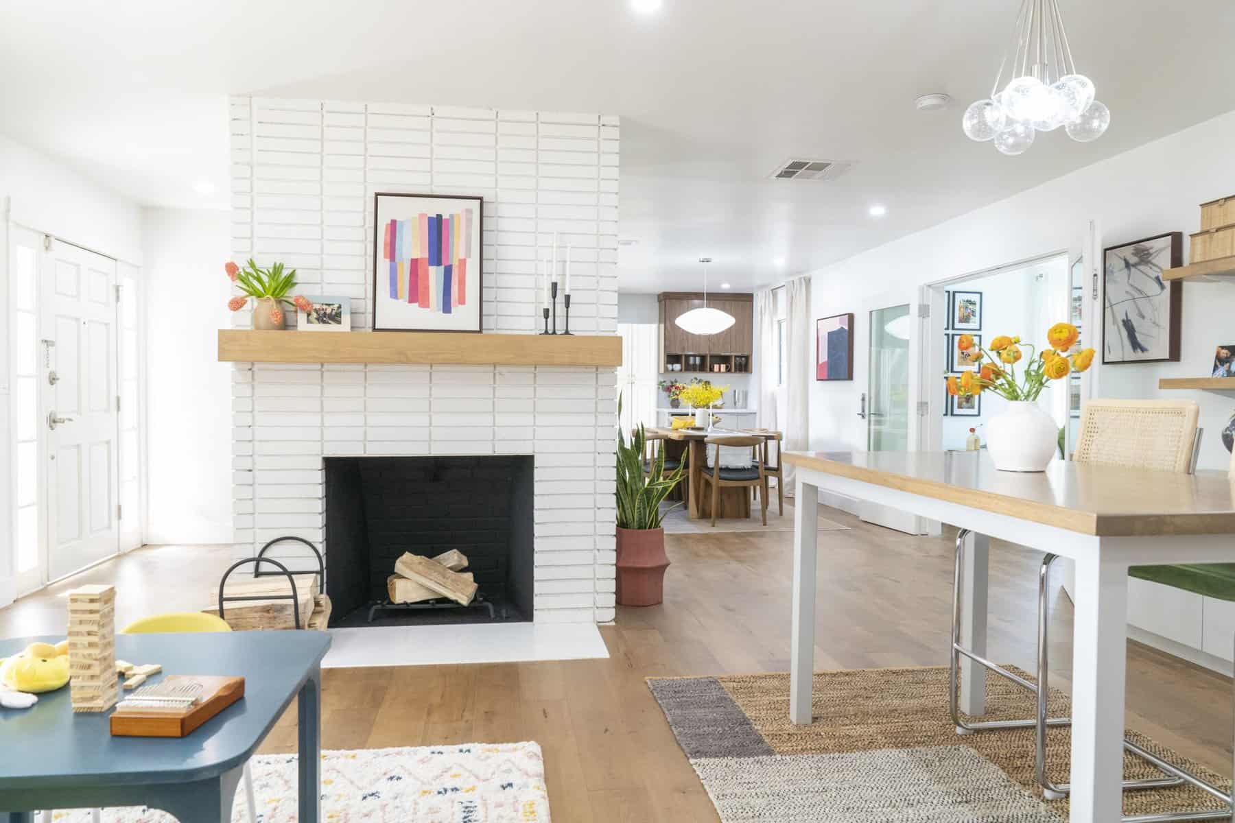 Bright open living space with a white brick fireplace, wood mantle, and modern decor accents