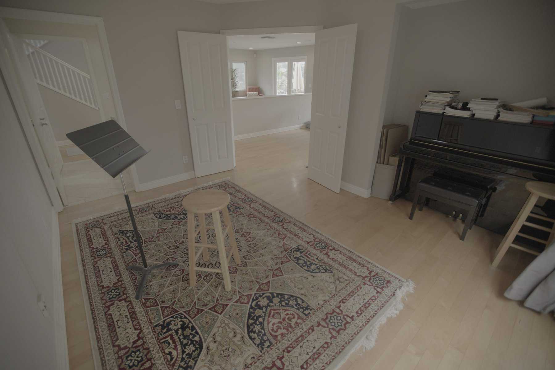 Music room with a black piano, sheet music, a music stand, and a patterned rug on a light wood floor
