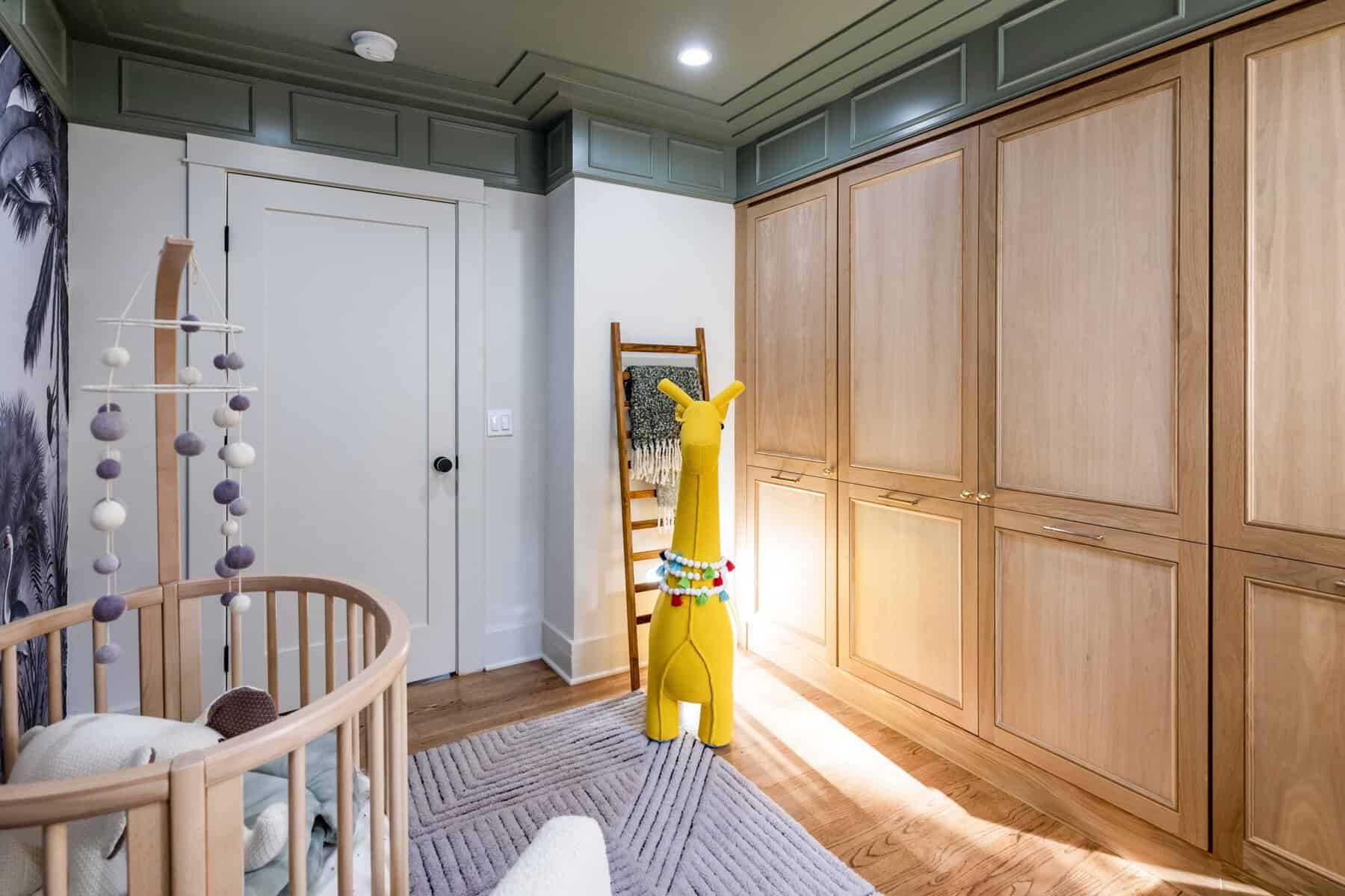 Cozy nursery with light wood crib, plush giraffe toy, soft rug, and built-in wood cabinets