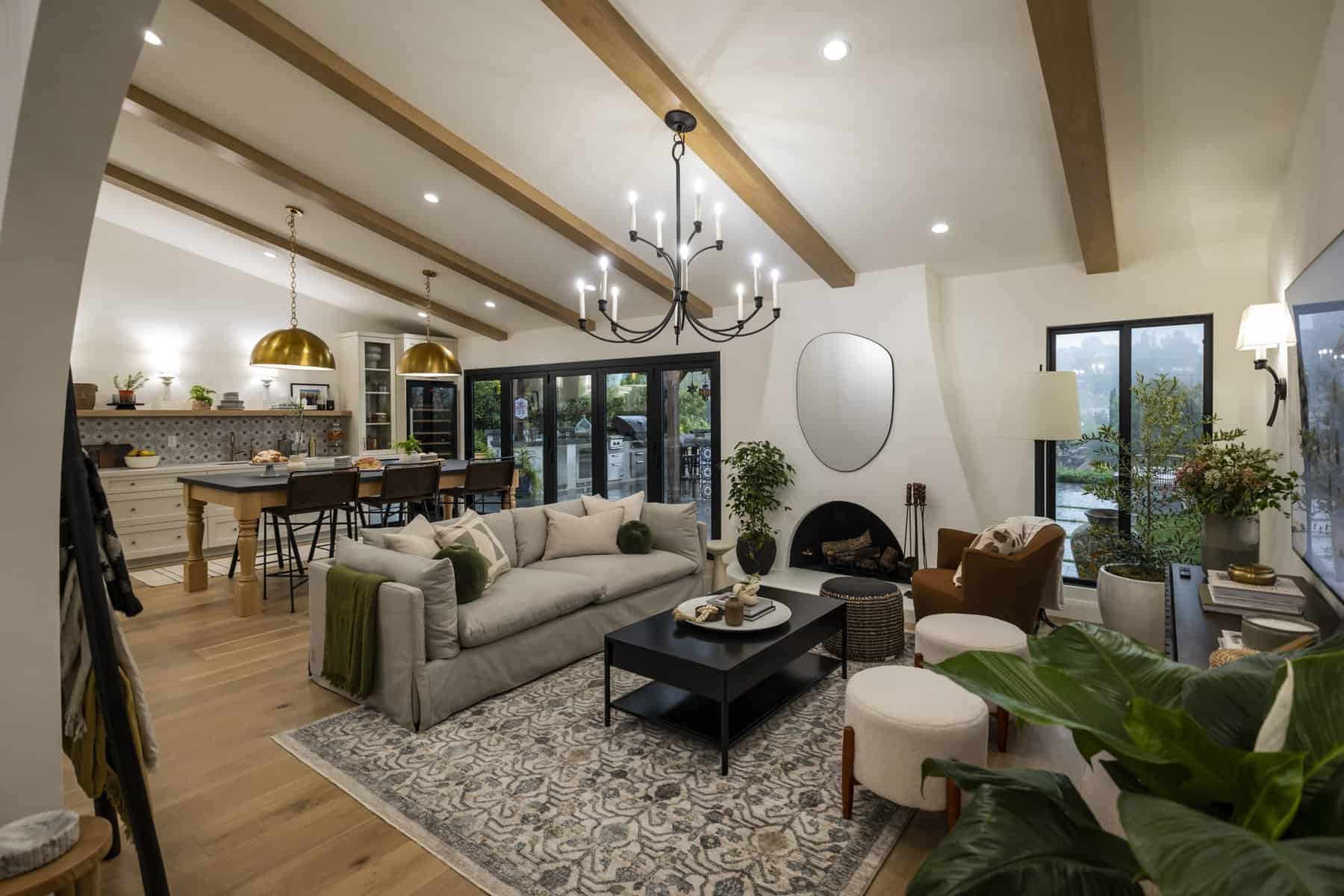 Warm and inviting open-concept living space with wood beams, a chandelier, and a cozy fireplace