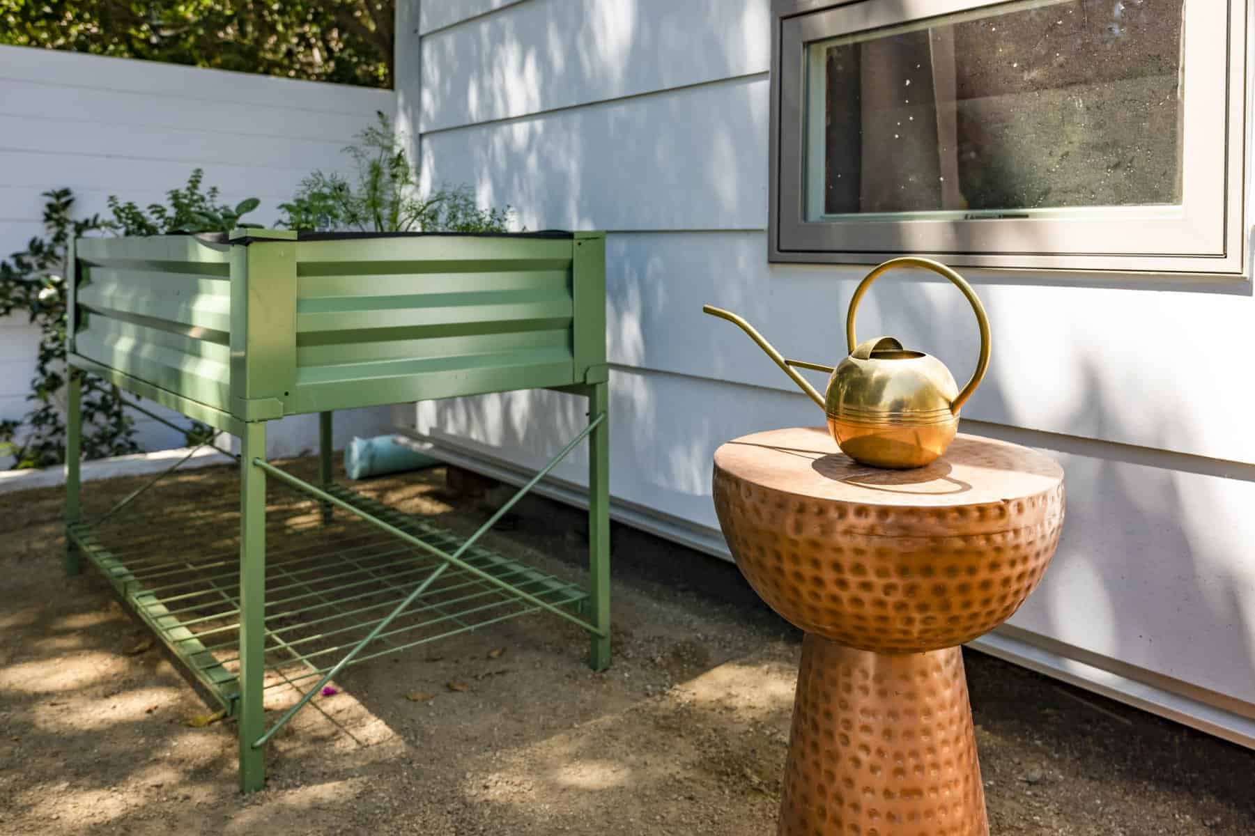 Outdoor planter box with herbs next to a copper side table holding a gold watering can