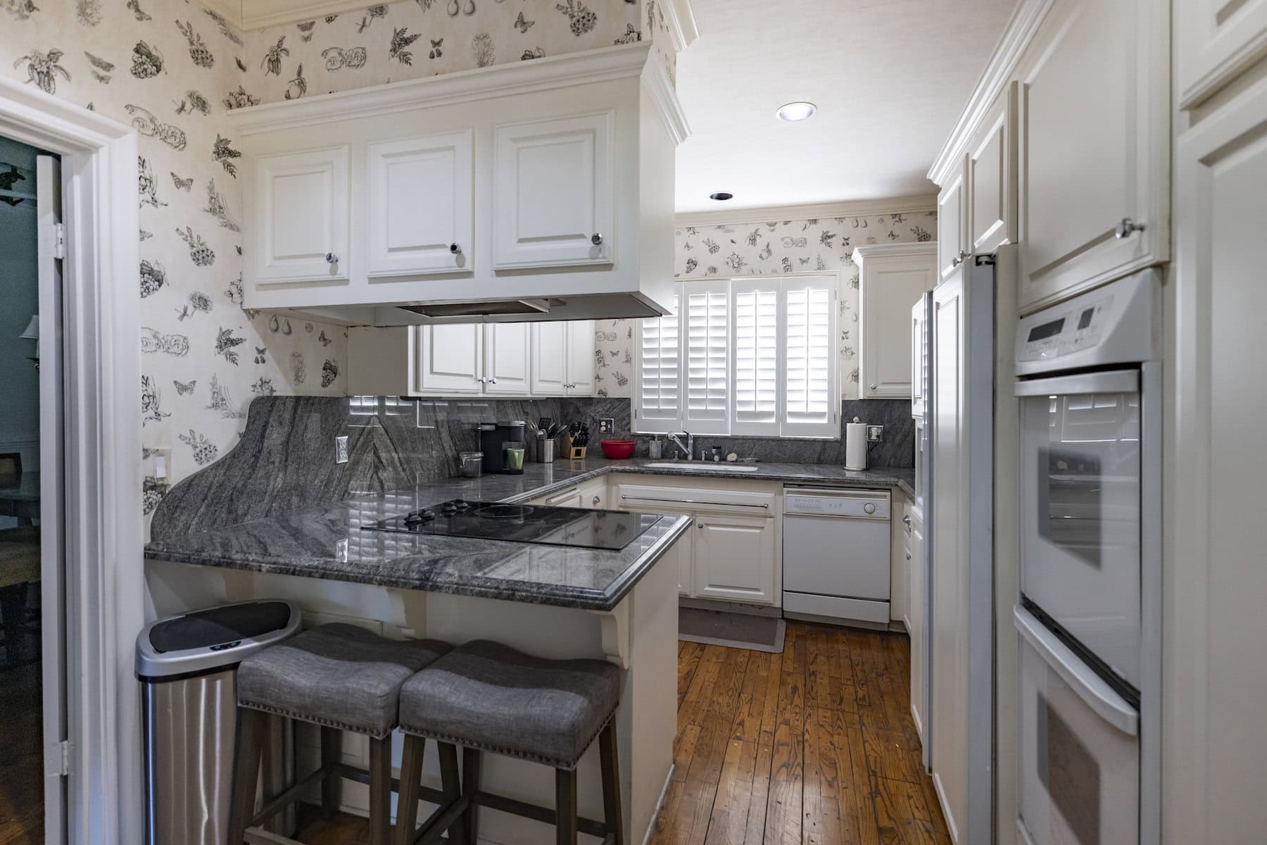 Traditional kitchen with white cabinets, gray marble countertops, double ovens, and floral wallpaper
