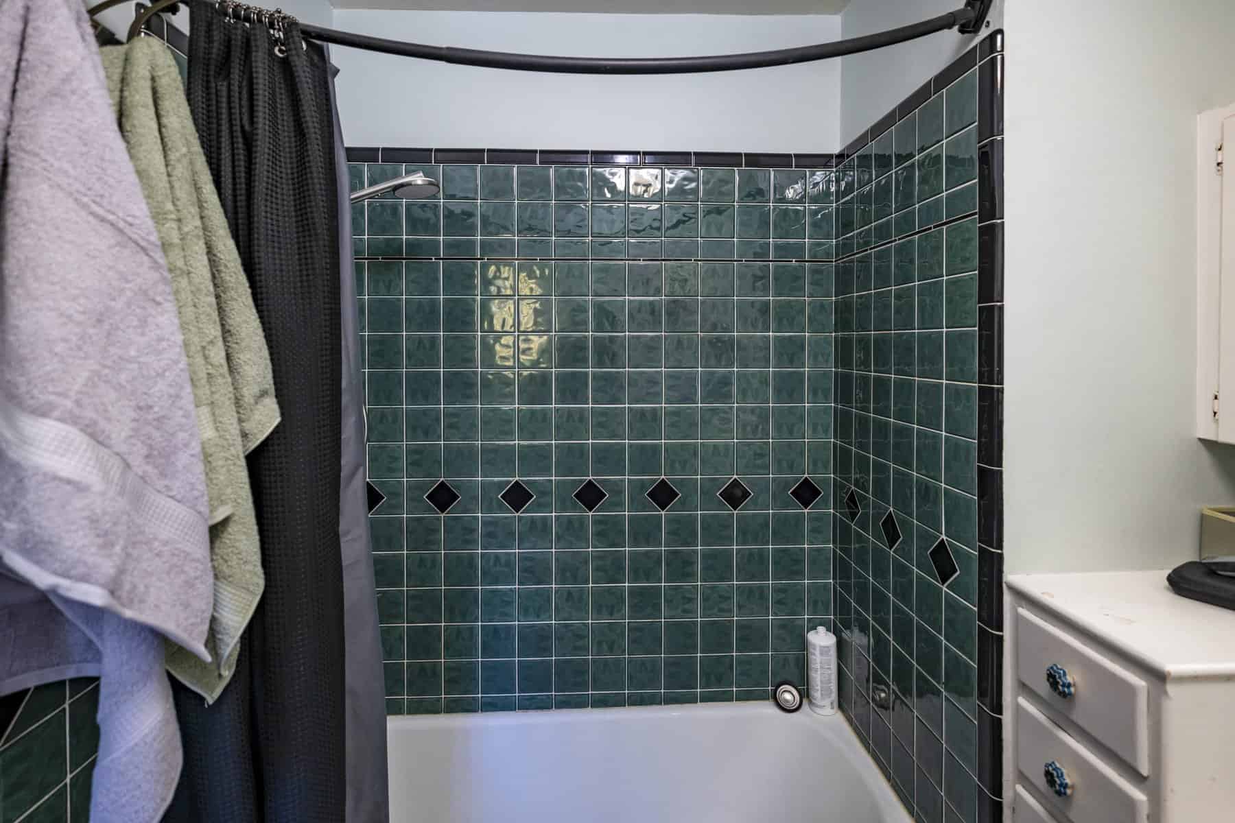 Shower with dark green square tiles, black diamond accents, and a curved curtain rod